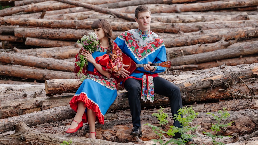 a man and woman sitting on a log holding flowers
