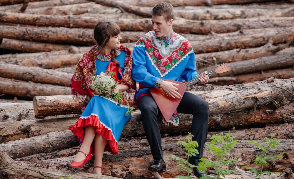 a man and woman sitting on a log holding flowers