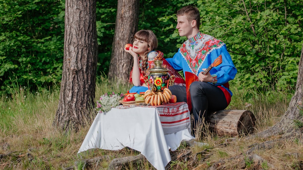 a man and a woman sitting on a blanket in the woods