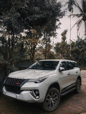 a white car parked on a dirt road with trees and a building in the background
