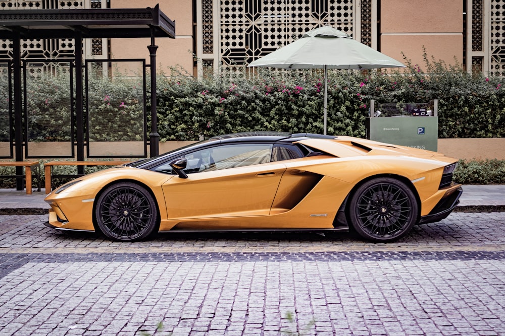 a yellow sports car parked on a brick road with an umbrella