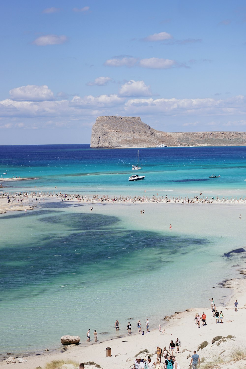 a beach with people and a large rock in the background