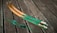 Two curved wooden objects with green and brown hues rest on a wooden plank surface. The items appear to be archery bow limbs with intricate patterns. A coiled green string with fluffy sections is positioned nearby.
