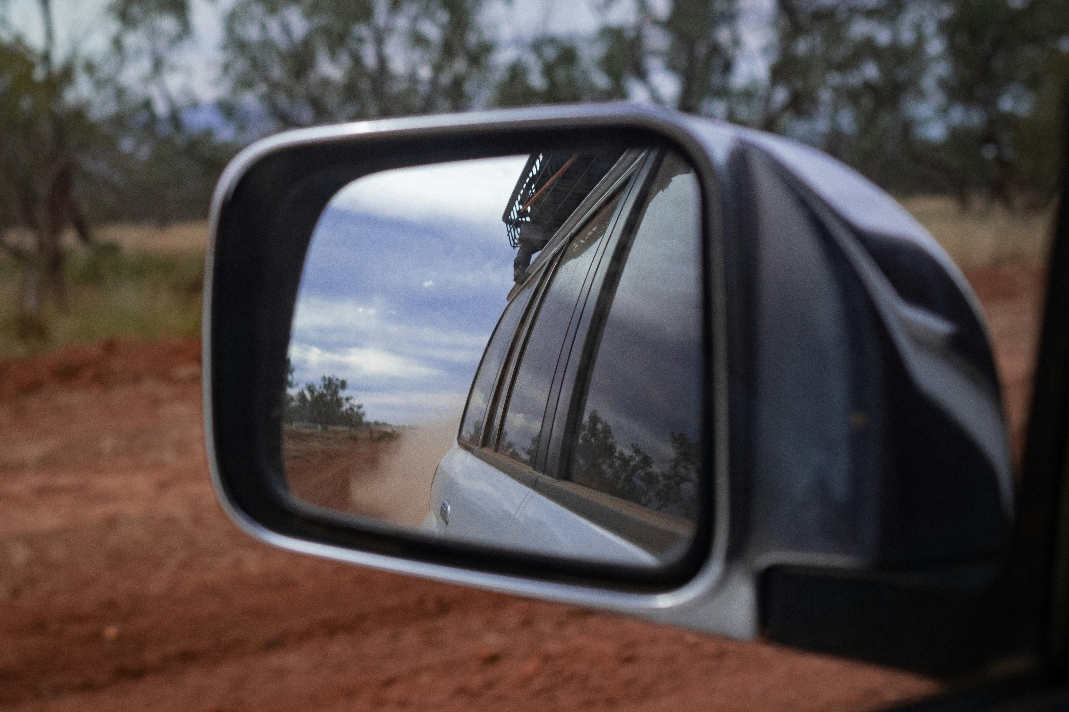 a side view mirror on a car, Looking in the rear view mirror on a red dirt road in outback Australia