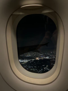 Nighttime cityscape viewed from an airplane window, city lights sparkling below.
