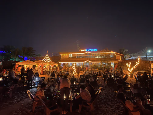Guests enjoying a lively night beach party under twinkling lights and stars.