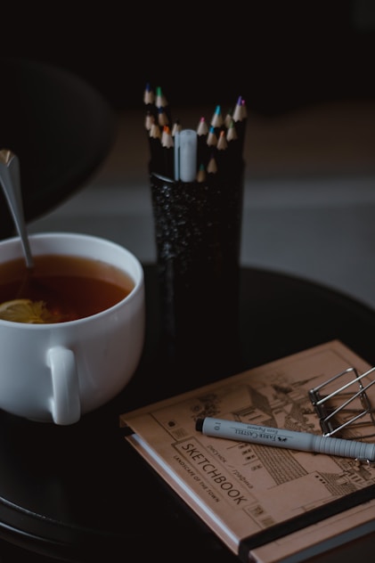A cozy workspace with printed coloring pages, colored pencils, and a steaming cup of tea.