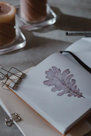 Close-up of a hand flipping through a beautifully illustrated notebook surrounded by soft, muted-toned candles.