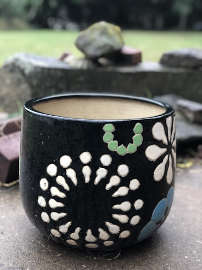 Close-up of a rugged, sturdy ceramic pot with a matte finish, sitting outdoors with fresh green foliage.