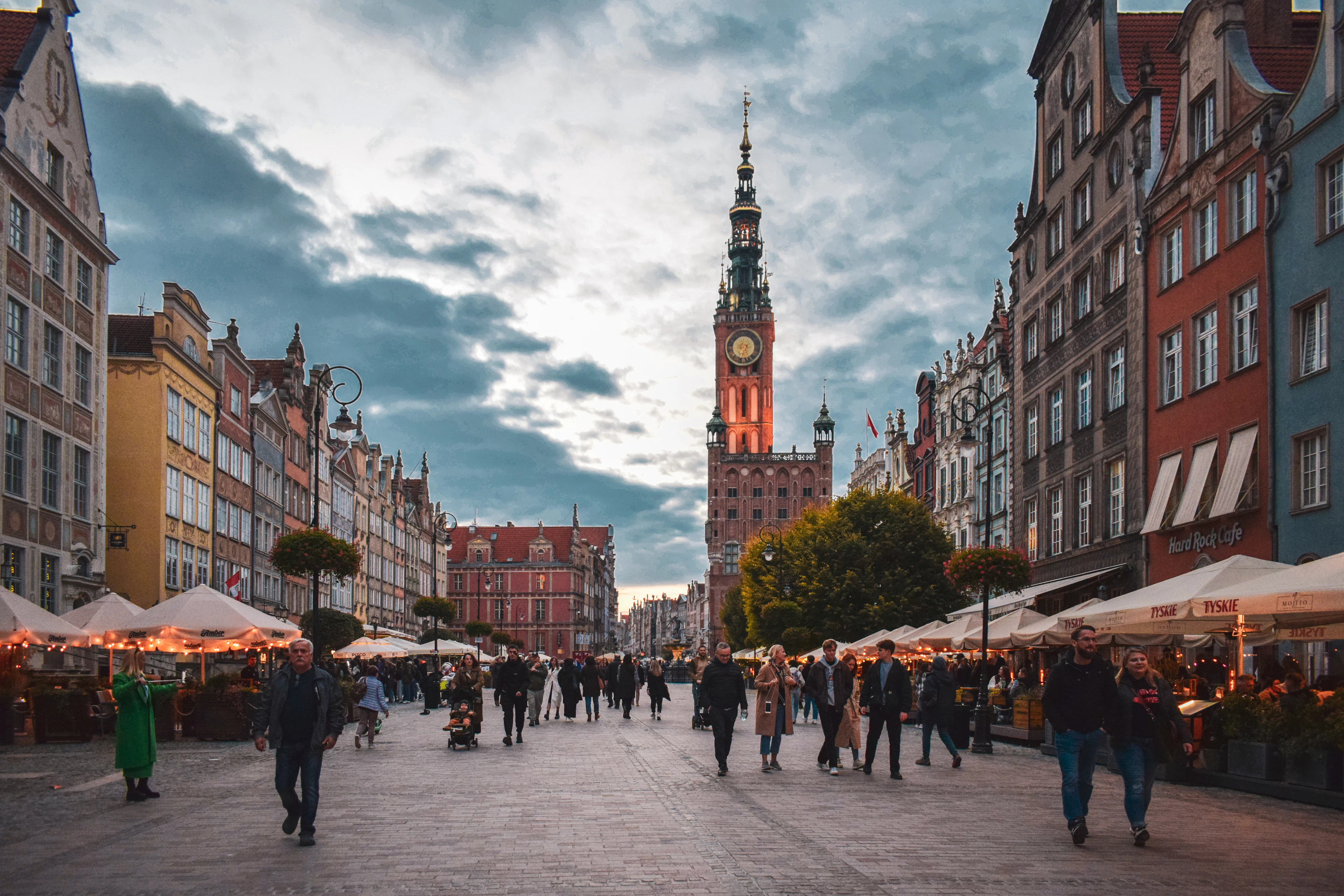 Dusk on Gdańsk's Long Market, market stalls and strollers beneath the glowing, lit-up Town Hall tower.