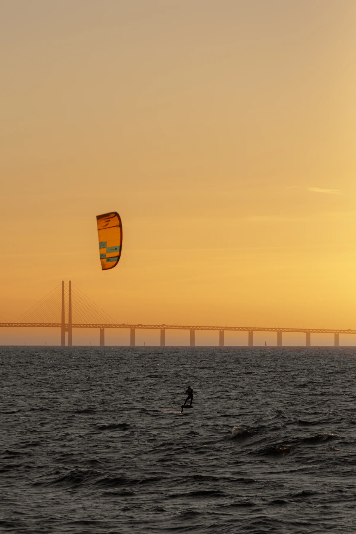 En kitesurfare i solnedgången med Öresundsbron vid horisonten.