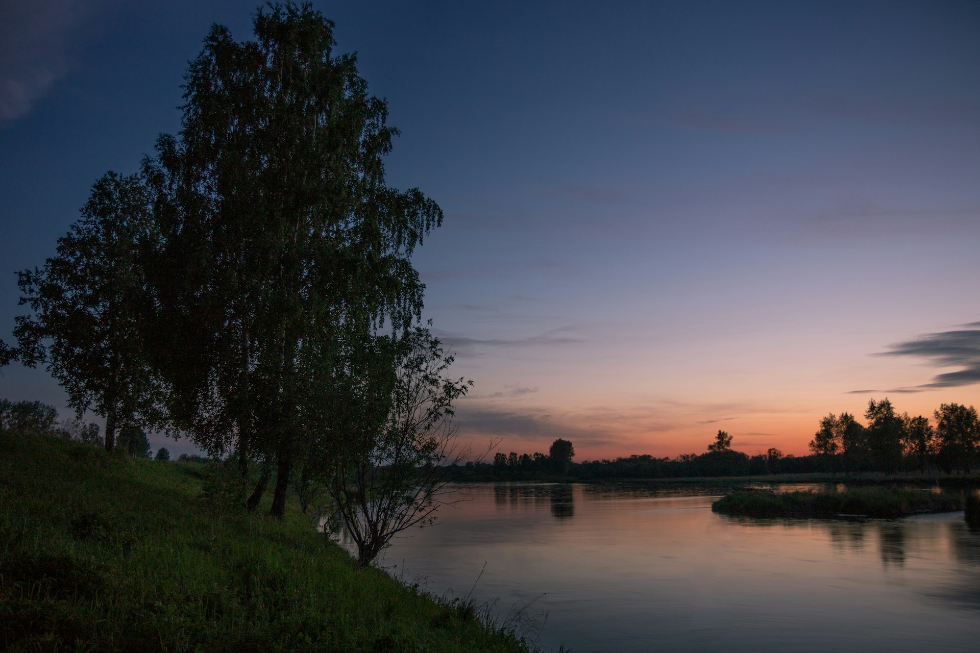 A peaceful riverside scene under a red sky, capturing the gentle reflection of morning colors on the water.