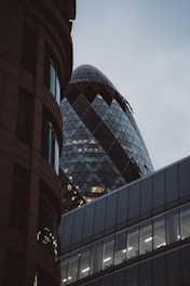 A modern architectural scene featuring distinctive skyscrapers. The image showcases a building with a unique curved glass facade and triangular patterns, partly obscured by darker, more traditional structures.