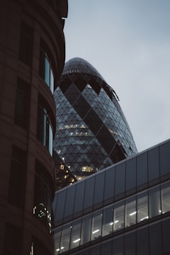 A modern architectural scene featuring distinctive skyscrapers. The image showcases a building with a unique curved glass facade and triangular patterns, partly obscured by darker, more traditional structures.