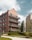 A modern residential building features multiple floors with balconies and a distinct brick façade. The structure is surrounded by lush greenery, including trees and well-manicured lawns. The sky is partly cloudy and adds a serene backdrop to the urban environment.