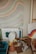A desk area filled with various art projects and supplies, including a poster with curved, colorful lines, rolls of decorative tape, notebooks, and cardboard cones. There are sheets with abstract designs, with one featuring bold, wavy lines in shades of orange, yellow, and pink.