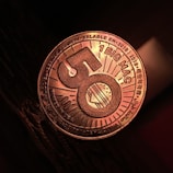 A close-up view of a coin-like token that has the number 50 prominently displayed in the center with a burger illustration. The words '1 BIG MAC' and various other texts in multiple languages can be seen around the edges. The token has a metallic sheen, and it is resting on a dark textured surface.