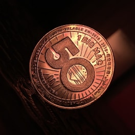 A close-up view of a coin-like token that has the number 50 prominently displayed in the center with a burger illustration. The words '1 BIG MAC' and various other texts in multiple languages can be seen around the edges. The token has a metallic sheen, and it is resting on a dark textured surface.