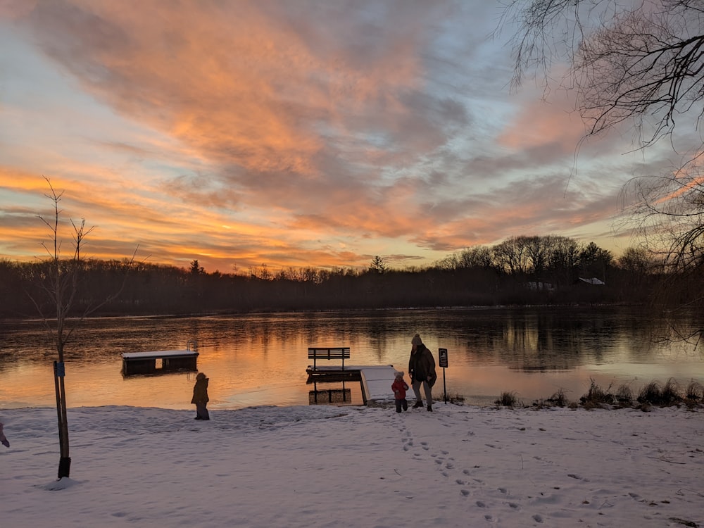 a group of people standing on a snowy field by a lake