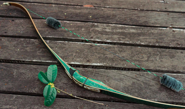 A close-up of weathered hands gripping a bow, set against a backdrop of autumn leaves.