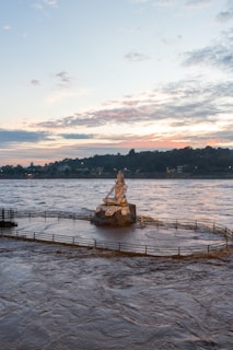 A serene statue of Lord Shiva meditating by the river under a twilight sky.