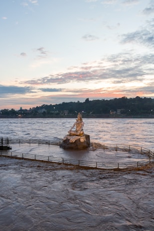 A serene statue of Lord Shiva meditating by the river under a twilight sky.