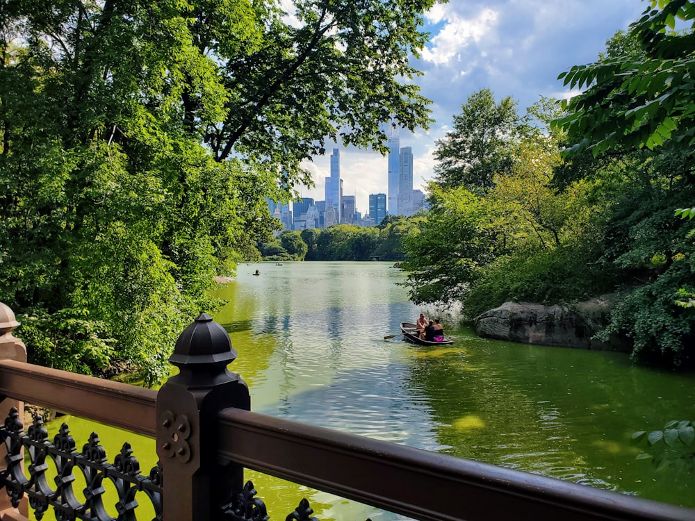 a couple people in a boat on a river with trees and a city in the background