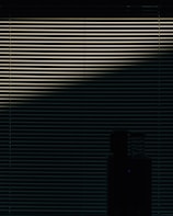 Horizontal blinds are partially open, allowing a dim light to pass through, casting a pattern of lines across the scene. In the lower part of the image, a silhouetted object is visible, possibly a piece of furniture or appliance.