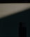 Horizontal blinds are partially open, allowing a dim light to pass through, casting a pattern of lines across the scene. In the lower part of the image, a silhouetted object is visible, possibly a piece of furniture or appliance.