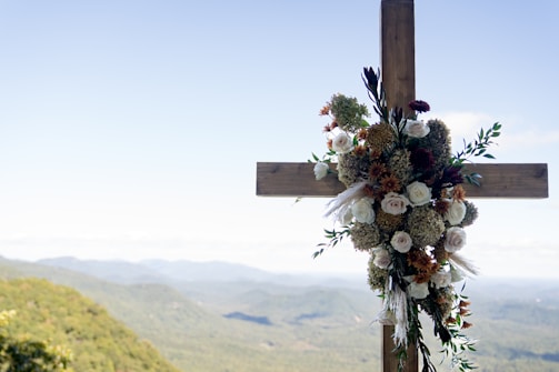 A close-up of a hand-carved wooden cross surrounded by fresh lilies.