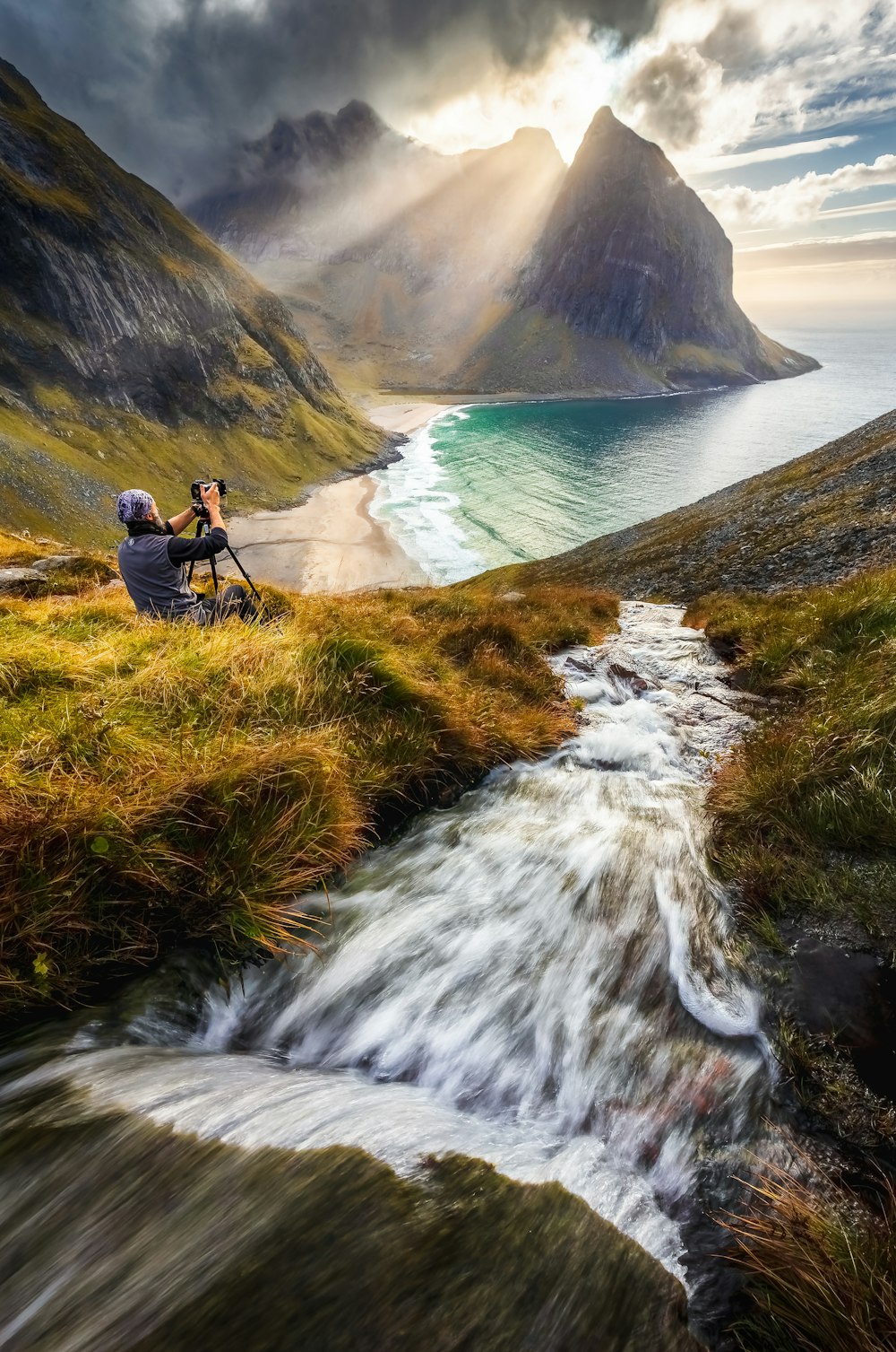 a person with a camera on a mountain by a body of water