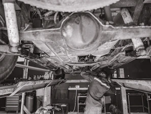 Mechanic working under a car lift with vibrant workshop colors of black, red, and white in the background.