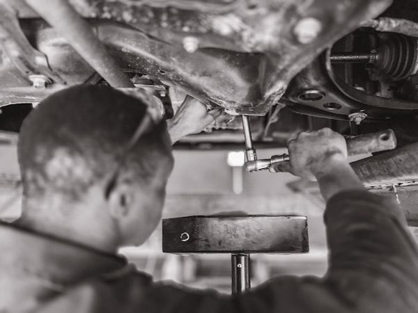 A picture of a man removing an oil sump plug to release old vehicle oil