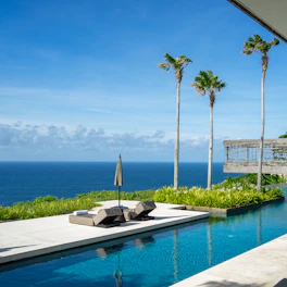 Private infinity pool beside the ocean villa with sun loungers and palm trees.