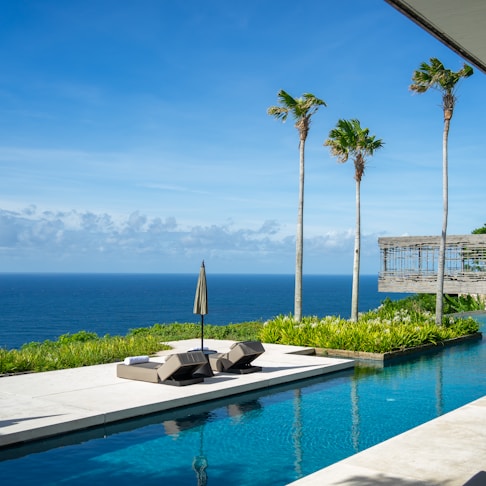 a pool with a lounge chair and umbrella by a body of water