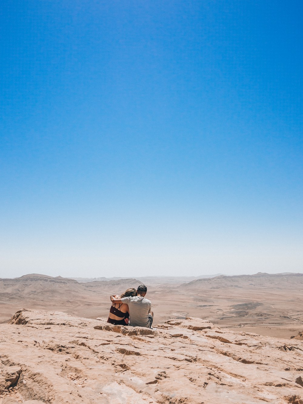 a man and woman sitting on a sandy hill