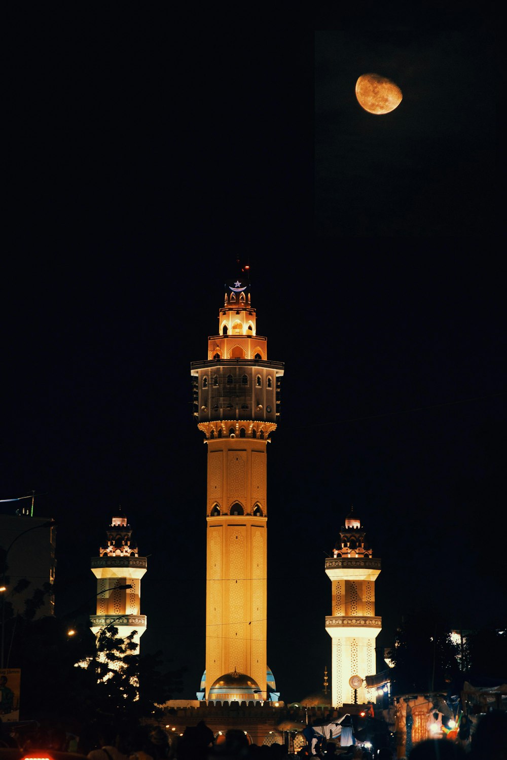 a tall building with a lit up top and a moon in the sky