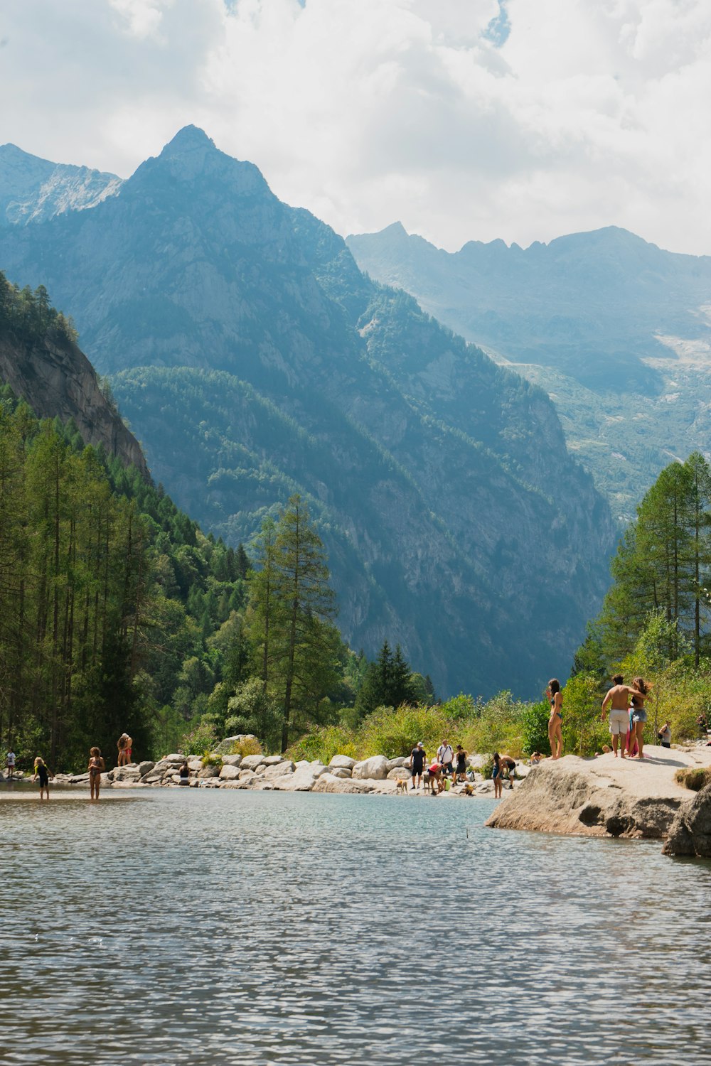 a group of people standing on rocks by a body of water with a mountain in the background