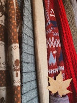 A collection of knitted sweaters in various textures and patterns, with earthy and autumnal colors. There is a maple leaf tucked into one of the sweaters, adding to the autumnal theme.