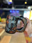 Close-up of a hand holding a warm, hand-thrown ceramic mug with a bright glaze.