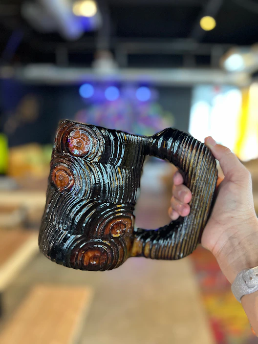 A close-up of a hand-thrown ceramic mug with earthy glaze tones resting on a wooden table.