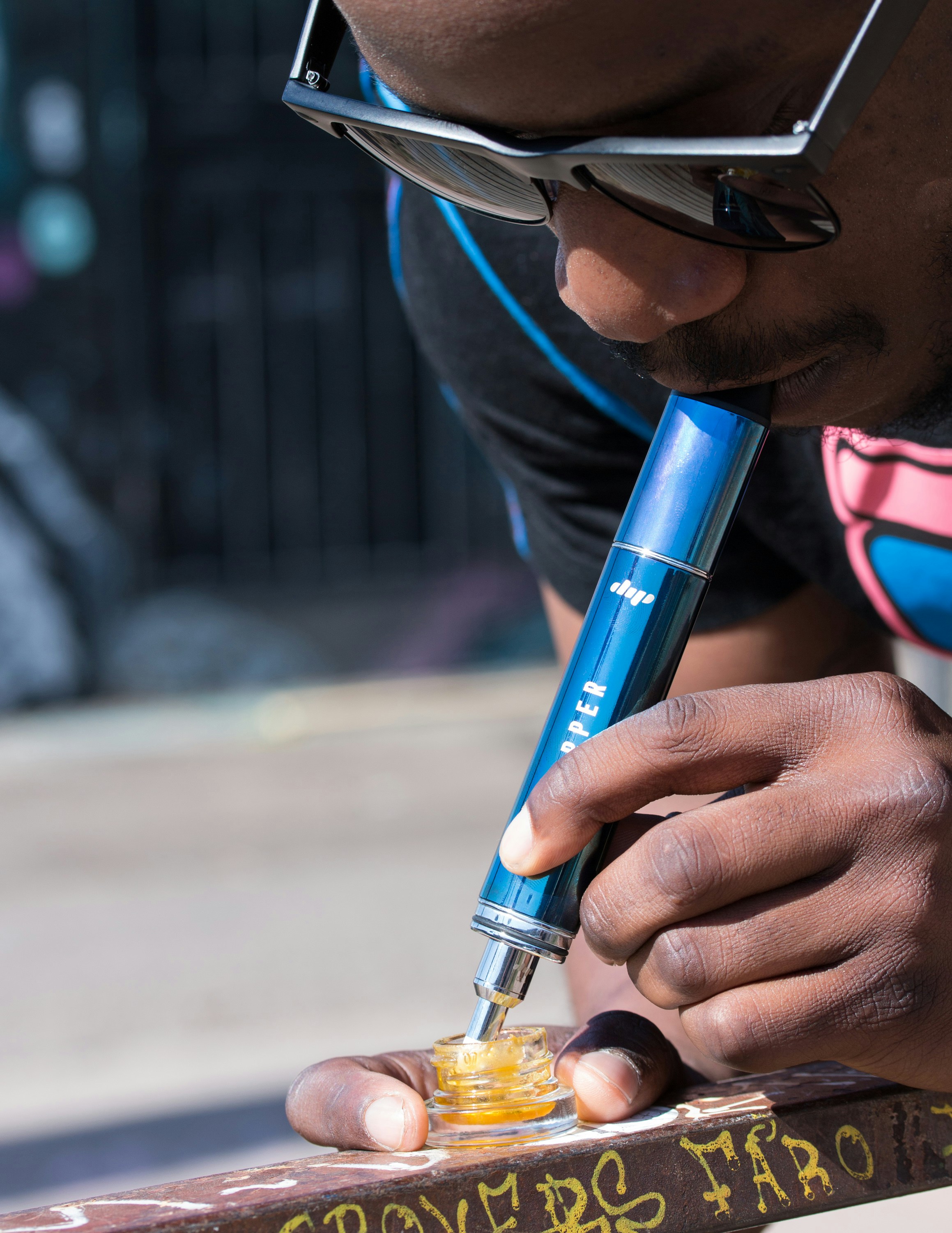 A man wearing sunglasses uses a blue Dip Devices Little Dipper dab pen to consume cannabis concentrates. Get your dab straw at https://dipdevices.com/