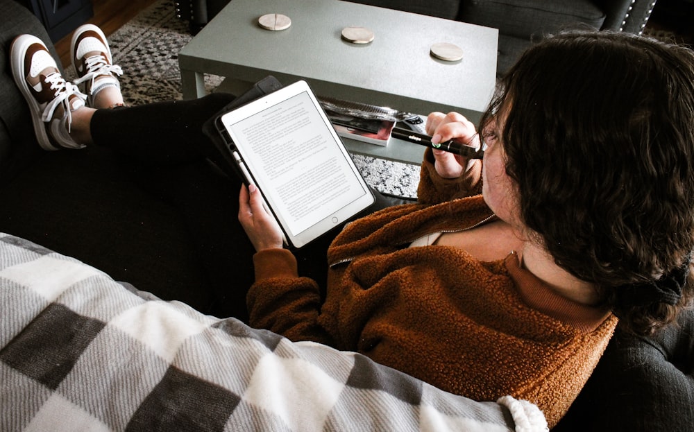 Eine Person, die mit einem Tablet und einem Laptop auf einer Couch sitzt