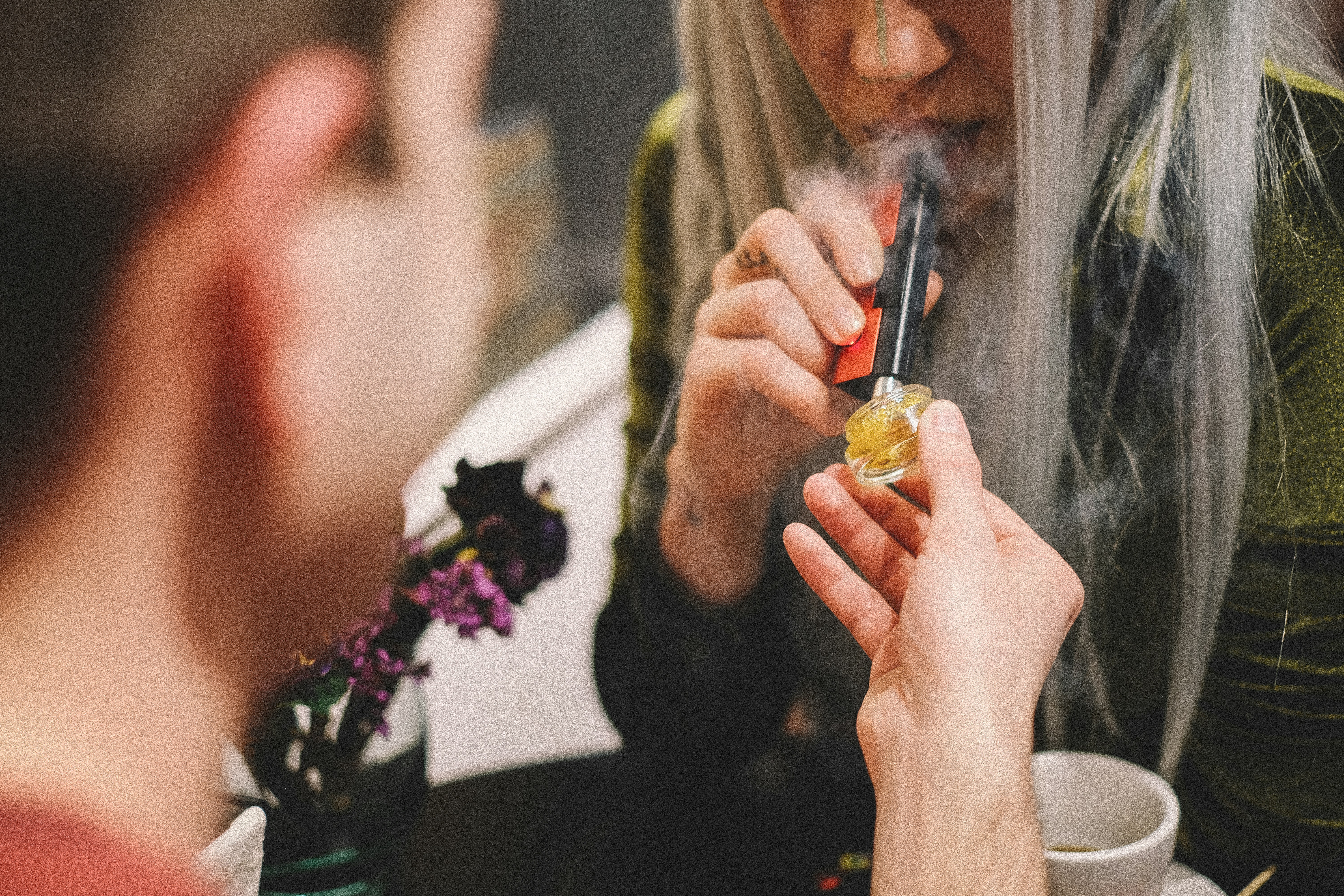 A man holds out cannabis concentrates to a tattooed woman who uses a Dip Devices EVRI 3-in-1 multifunction vape pen and electric dab straw to smoke. Get yours at https://dipdevices.com/