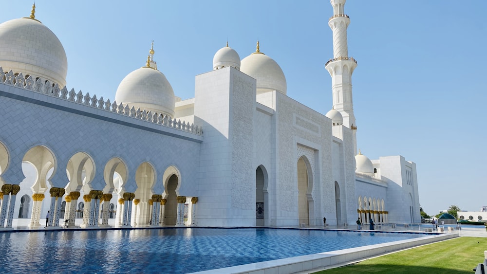 a large white building with domes and towers by a body of water with Sheikh Zayed Mosque in the background