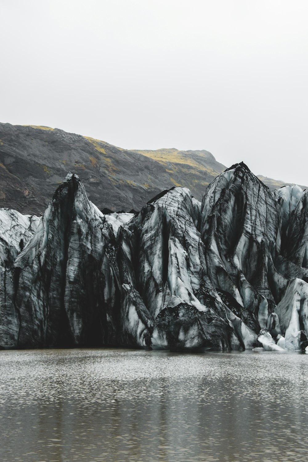 a body of water with a rocky cliff and a mountain in the background