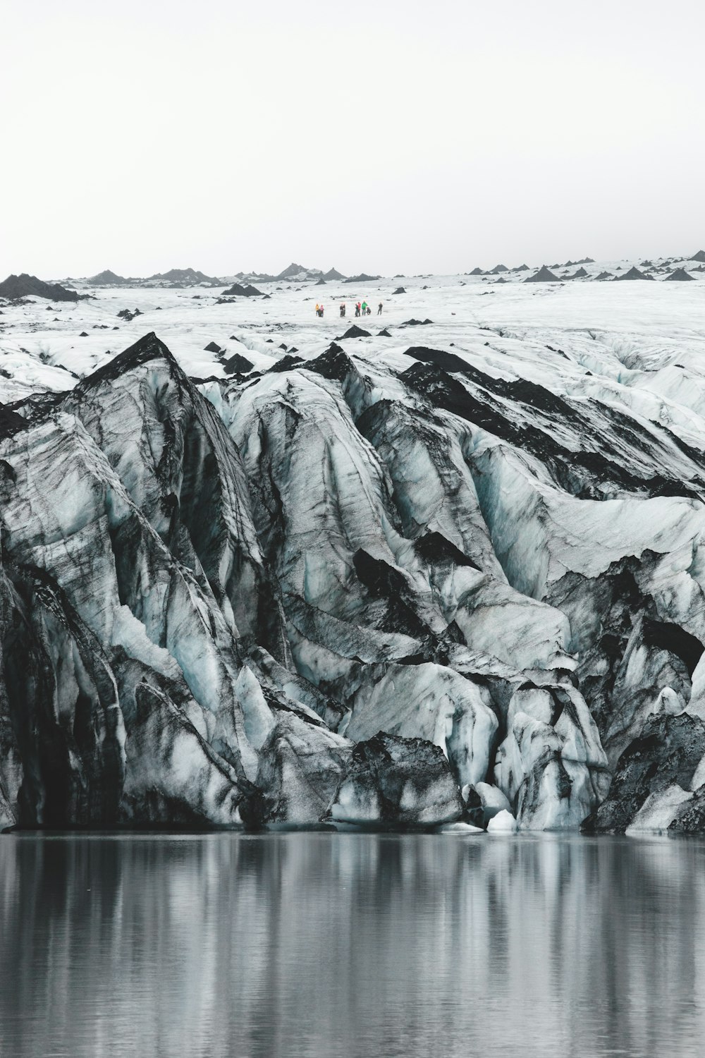 a body of water with a rocky cliff and a snowy mountain in the background