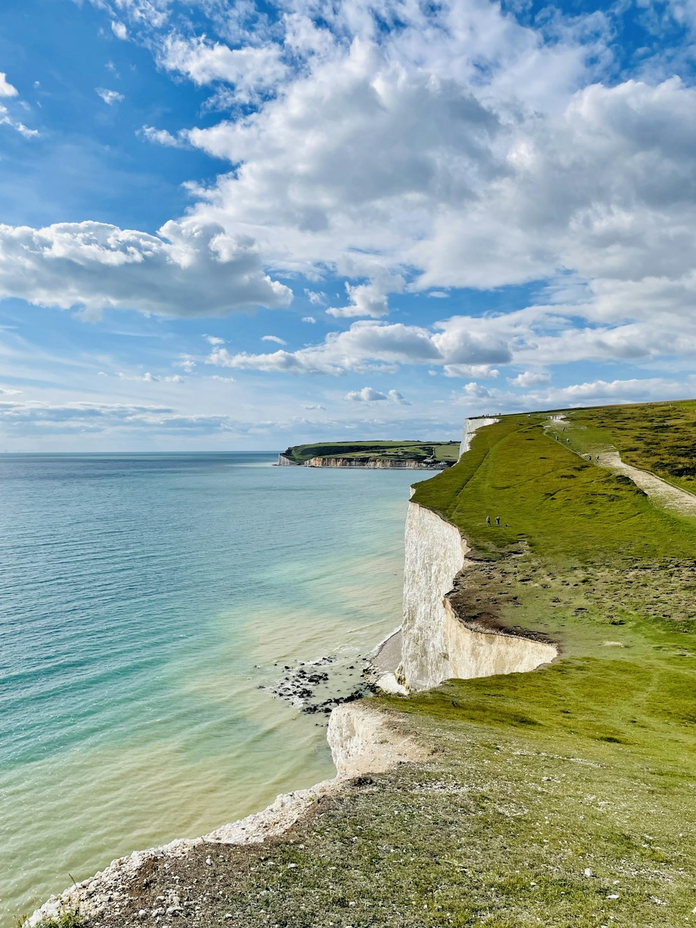 a beach with a body of water and land with a land with a hill and a blue sky