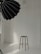 A minimalist studio setup with a tall stool positioned against a white brick wall. A large black photography umbrella is partly visible, casting light onto the scene. The floor is smooth and reflective, creating a clean and bright atmosphere.