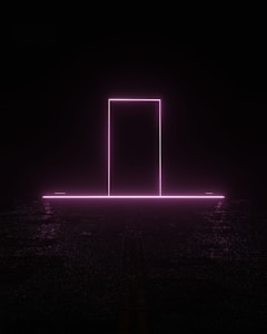 A neon pink rectangle resembling a doorway stands illuminated against a dark background. The glow from the neon light reflects subtly on the ground, creating an ethereal and futuristic atmosphere.
